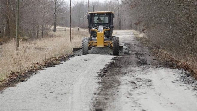 A grader is used to convert a paved section of road to gravel in Nashville, Indiana. Faced with tight budgets, some communities are converting roads to dirt instead of repaving them.