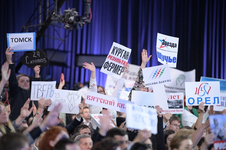 Journalists at an annual news conference by Russia's President Vladimir Putin. The yearly event features over a thousand journalists clamoring to ask a question, some bringing signs to draw attention to themselves.