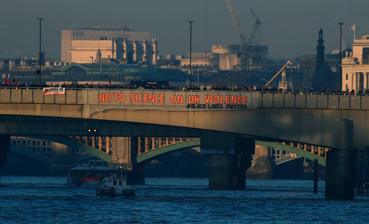 Demonstrators hang a banner that reads "No To Silence On UK Violence" from London Bridge.