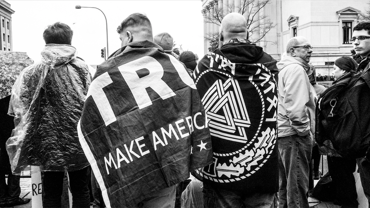 The Trump supporter on the right is draped in a flag with Aryan runes and a Neo-Nazi symbol called a “Valknot.” 