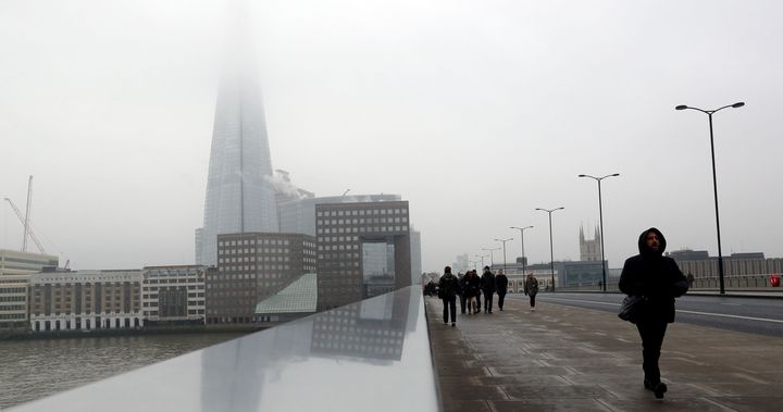 Pedestrians cross London Bridge with the Shard shrouded in fog behind them