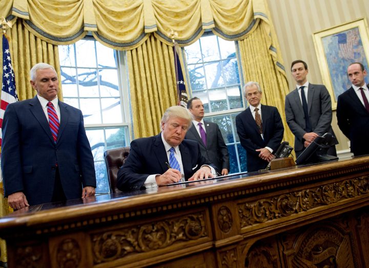 <strong>(Left) Pence looks over Trump's shoulder as he signs the executive order</strong>