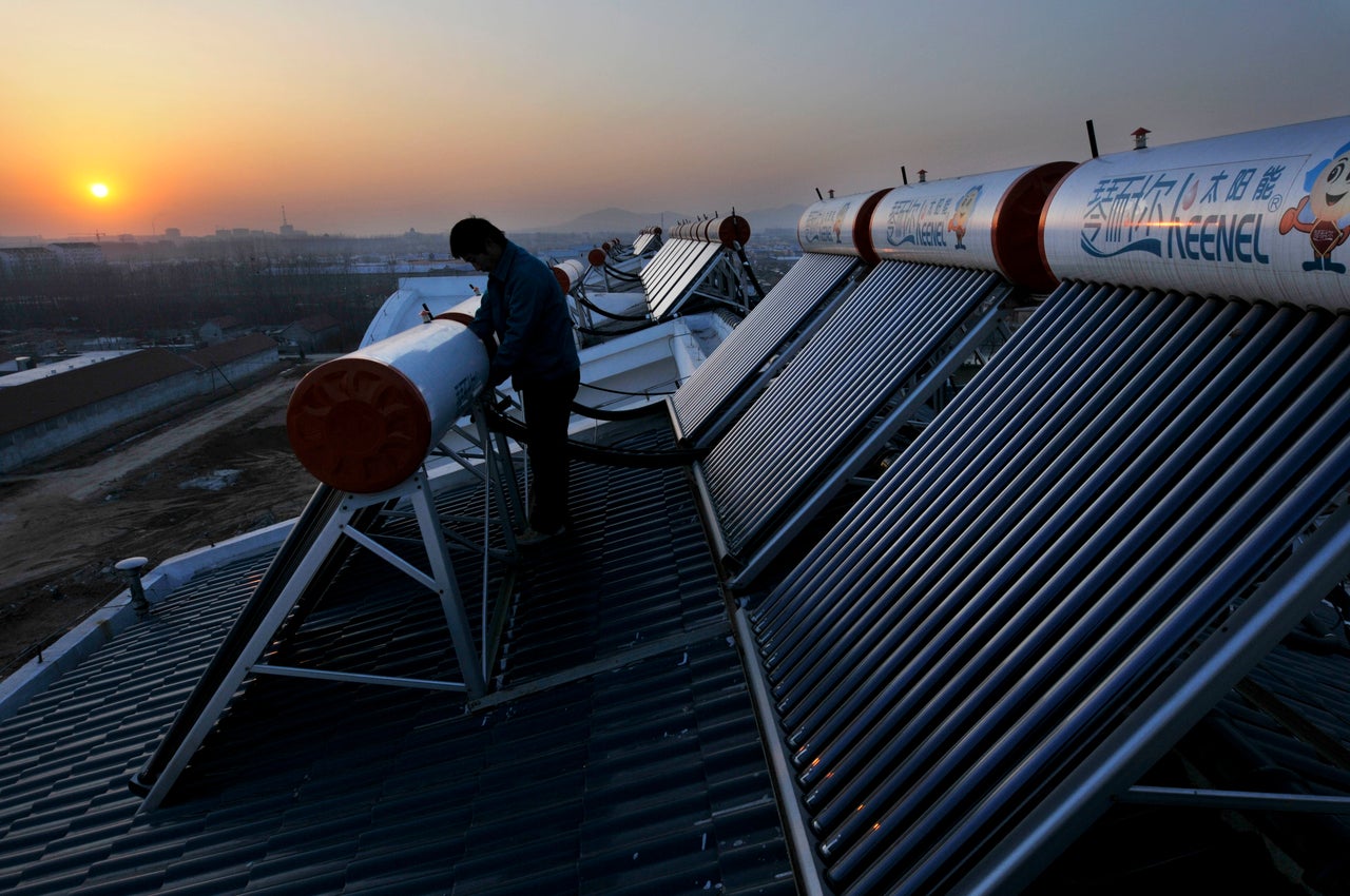 Workers install solar heaters on the roof of a house in Rizhao. Dec. 21, 2009.