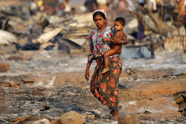 A woman carries a baby past shelters for internally displaced Rohingya Muslims in Myanmar that were destroyed in a fire.