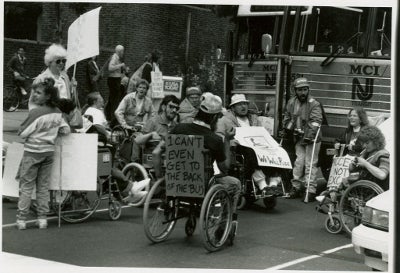 <p><strong>People with a range of disabilities publicly protesting in front of a bus in the 1970s, before the Americans with Disabilities Act was passed. One man in a wheelchair has a sign that reads, “I can’t even get to the back of the bus.”</strong></p>