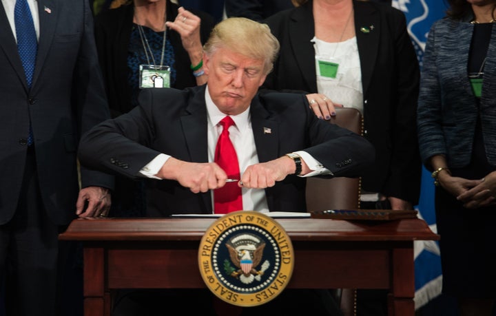 US President Donald Trump takes the cap off a pen to sign an executive order to start the Mexico border wall project at the Department of Homeland Security facility in Washington, DC, on January 25, 2017.