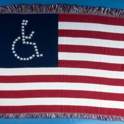 An American Flag blanket sewn by disability rights activists from the ADAPT group. The normal fifty stars are placed in the shape of a person in a wheelchair.  