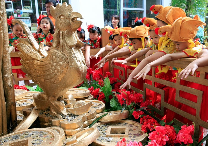 Filipino-Chinese students with rooster hats gesture after tossing a coin in front of a Prosperity Tree display, which is beli