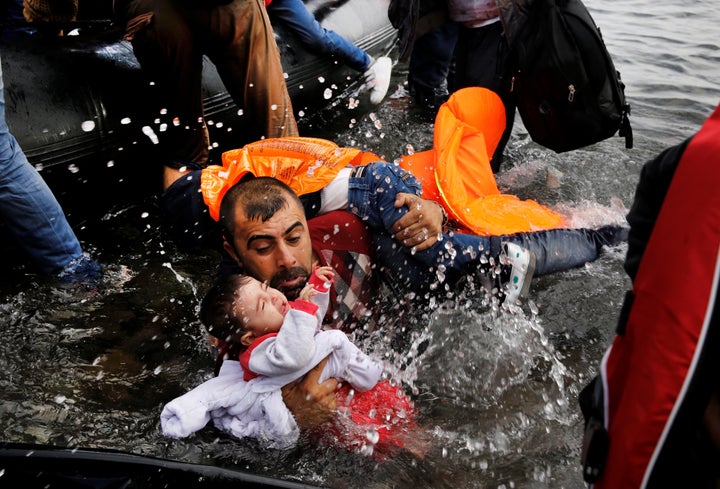 A Syrian refugee holds his two children as he struggles to disembark from a raft on the northern coast of the Greek island of