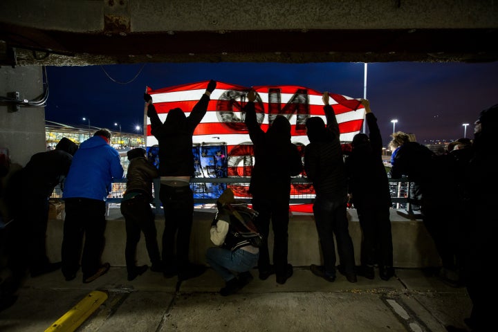 Demonstrators in a parking garage at JFK hold an upside-down American flag saying "no borders." 