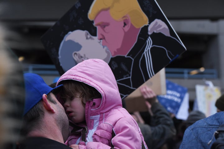 A man holds a child in front of a protest sign showing Donald Trump kissing Russian President Vladimir Putin.