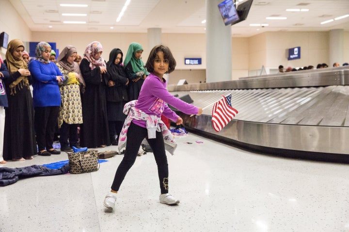 A young girl dances with an American flag in baggage claim at Dallas/Fort Worth International Airport on Jan. 29 while women pray behind her during a protest against the travel ban imposed by President Donald Trump's executive order.