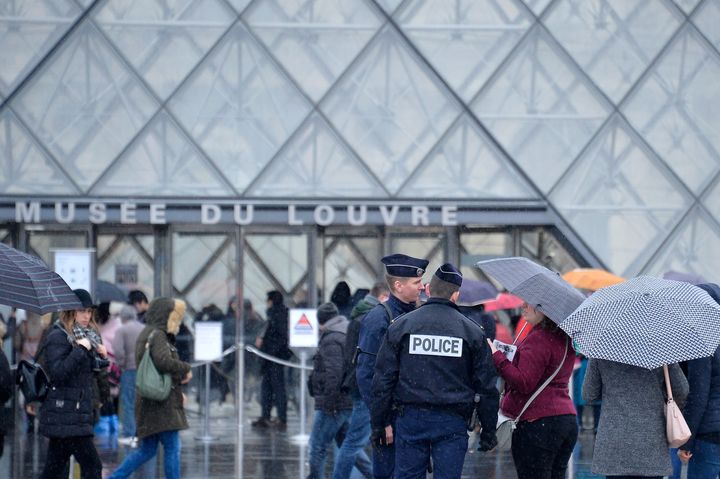 Police officers talk with tourists who are about to enter the Louvre which reopened on Saturday