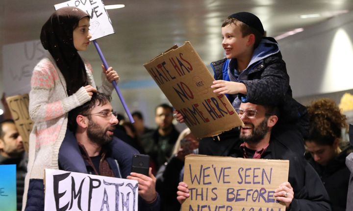Meryem Yildirim, 7, left, sits on her father, Fatih, of Schaumburg, and Adin Bendat-Appell, 9, right, sits on his father, Rabbi Jordan Bendat-Appell, of Deerfield, during a protest on Monday, Jan. 30, 2017 at O'Hare International Airport in Chicago, Ill.