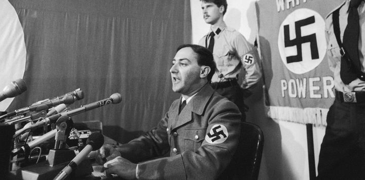 American Nazi leader Frank Collin, flanked by members of the National Socialist Party of America, speaks at a news conference in Skokie, Illinois. 1977.