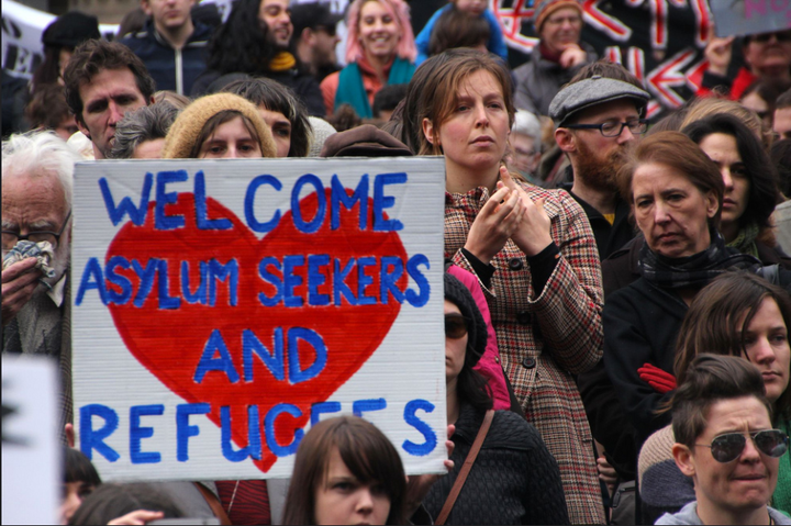 Demonstrators hold signs in support of asylum seekers at a rally supporting refugees.