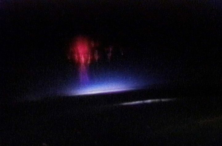 A red and blue flash of light called a Red Sprite, is shown extending upward from an electrical thunderstorm in this NASA photograph.
