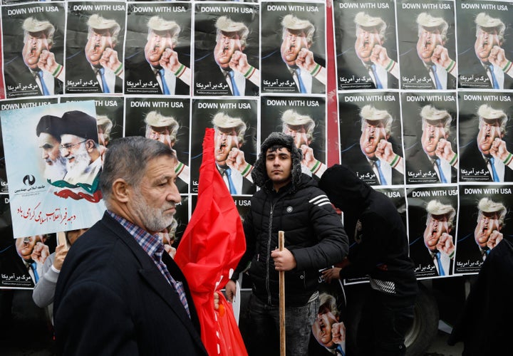 An Iranian man stands in front of placards showing a caricature of President Donald Trump during a rally marking the annivers