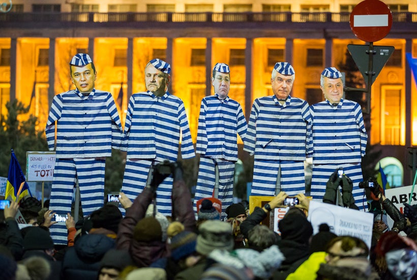 Protesters outside the government building in Bucharest hold up life-size cutouts of politicians in prison uniforms while cal