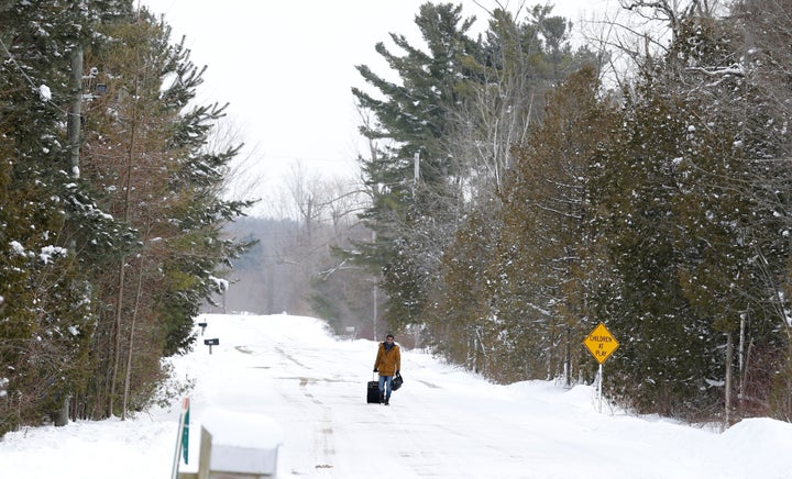 A man walks with his luggage down Roxham Road in Champlain, New York, toward the U.S.-Canada border in Hemmingford, Quebec, o