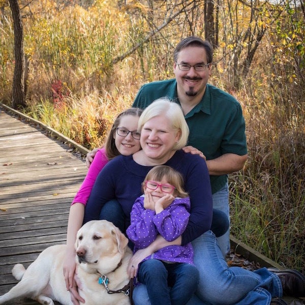 <p>Nicole Schultz-Kass, center, sits with her husband, Devin Kass, their daughters, Katie and Evie, and her retired guide dog, Picassa.</p>