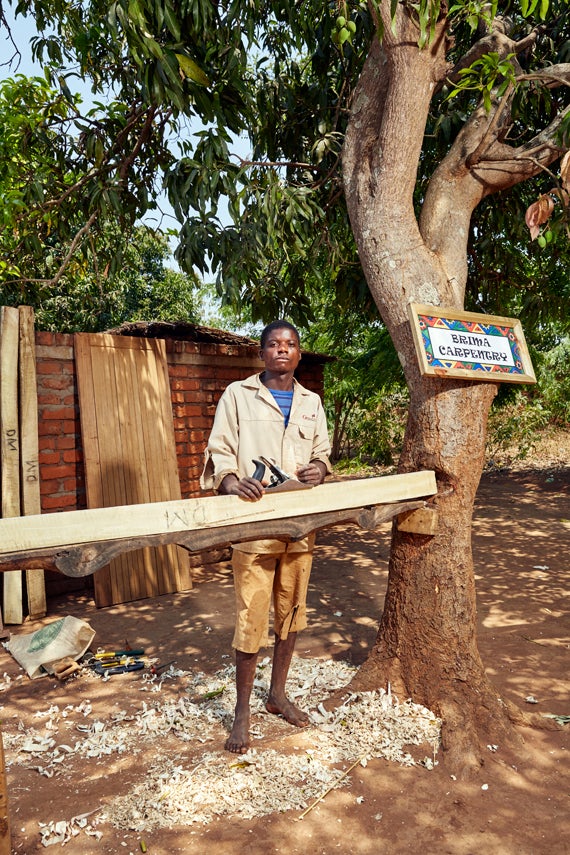 Laston Segula, 24 years old, stands in his carpentry workshop. Each entrepreneur decorates their stall or shop with a colourf