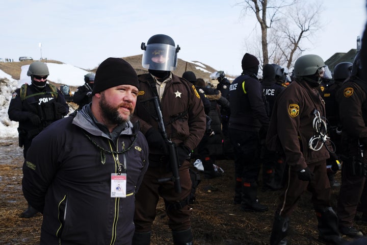 A man wearing a press ID steps in front of advancing law enforcement at the Ocetia Sakowin camp near a section of the Dakota Access Pipeline.