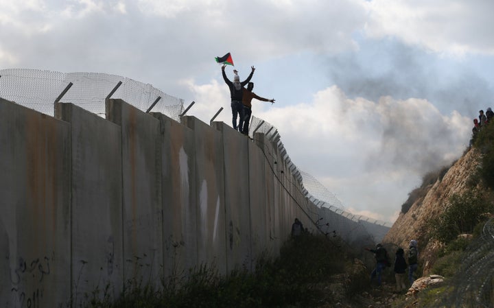 Palestinian protesters gesture as they climb an Israeli barrier in the West Bank village of Bilin near Ramallah on Feb. 17, 2017.