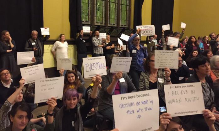 <p>Attendees of the kickoff event for the Pittsburgh chapter of Indivisible hold up signs with messages that include “I’m here because decisions are made by those who show up.”</p>
