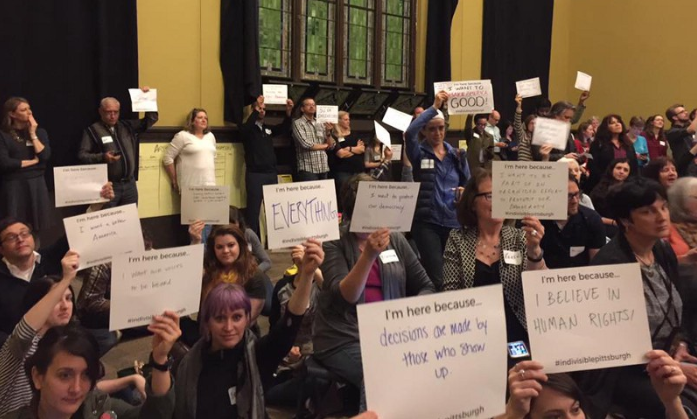 Attendees of the kickoff event for the Pittsburgh chapter of Indivisible hold up signs with messages that include “I’m here because decisions are made by those who show up.”