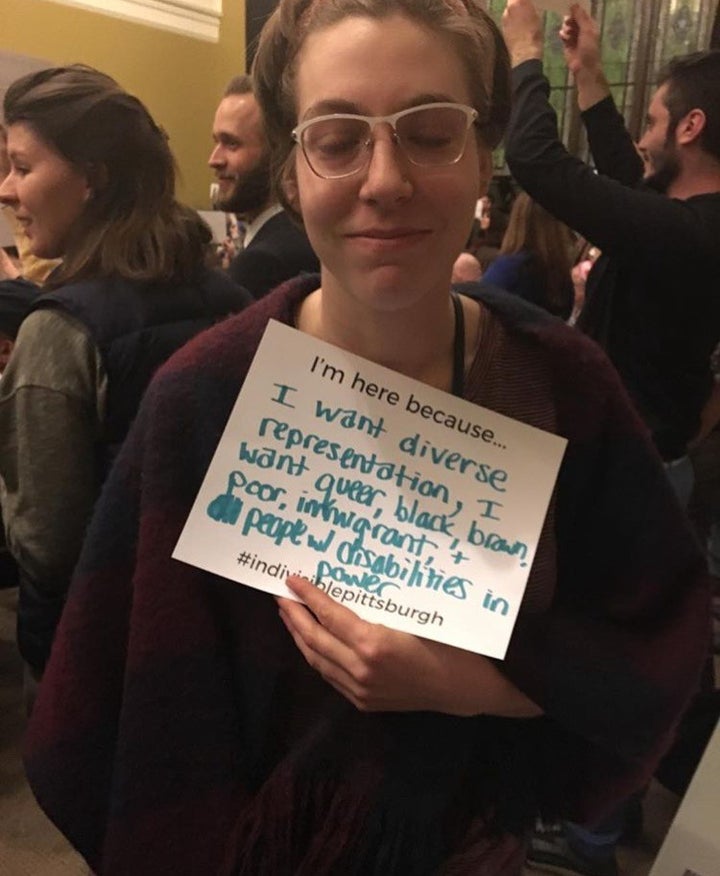 Queer artist Anna Nelson holds a sign that reads “I’m here because I want diverse representation, I want queer, black, brown, poor, immigrant, and people with disabilities in power.”