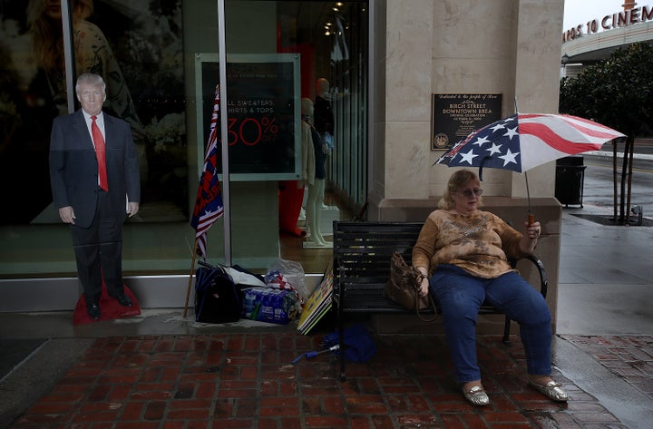 A Trump supporter with a cardboard cutout of the president sits on a bench at a rainy Brea, California, rally.