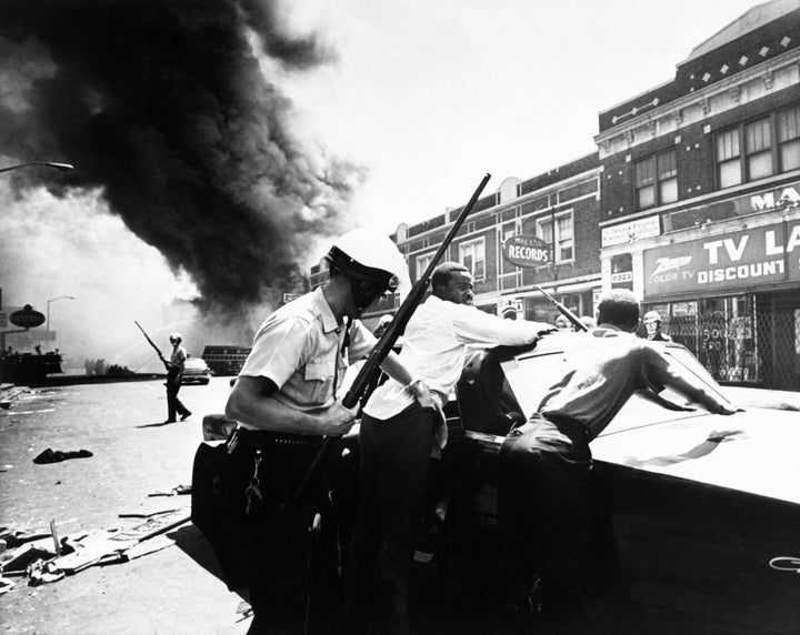 A police officers searches African-American men amid the turmoil of a Detroit street on July 25, 1967.