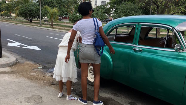Two women board a shared taxi (almendrón) in Havana.