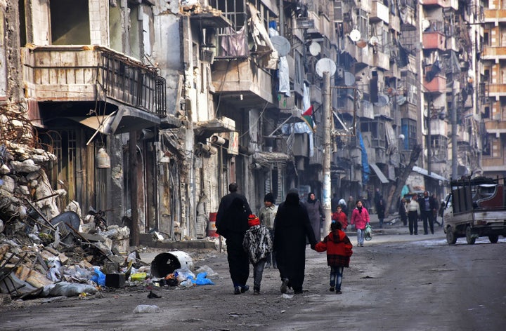 Syrians walk along a damaged street in Aleppo's formerly rebel-held al-Shaar neighborhood. 