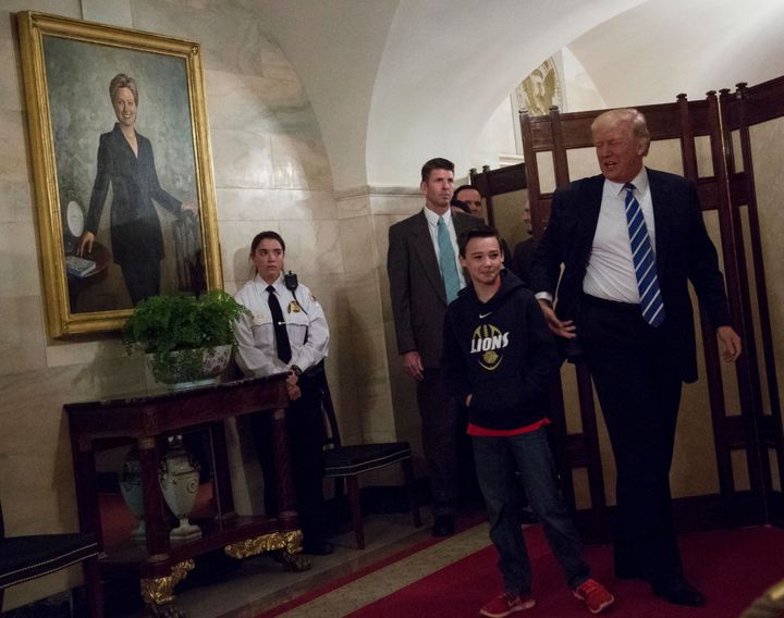 President Donald Trump greets Jack Cornish, 10, a White House visitor in a corridor of the White House while a portrait of Hillary Clinton hangs on the wall.