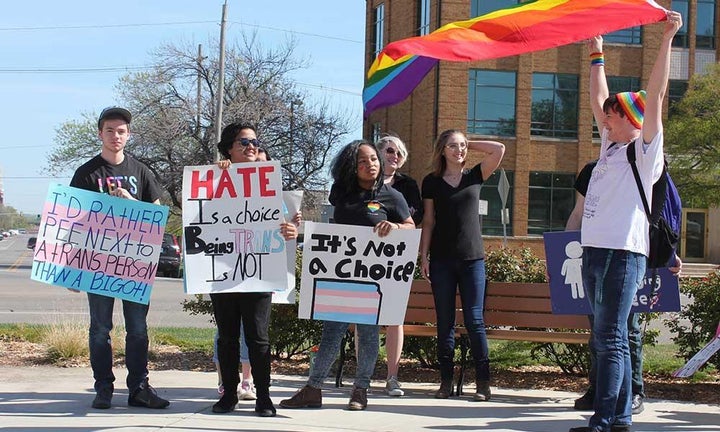 Six Kansas students hold signs supporting transgender rights. One is waving a large rainbow flag.