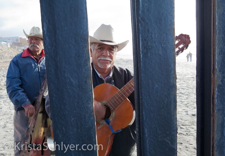 Musicians playing on the beach in Tijuana, seen through the border wall at a location designated as Friendship Park in the 1970s.