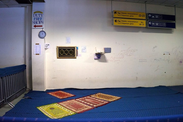 Prayer mats under the old Duty Free signs at the former Athens airport, now a refugee camp.