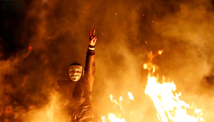 An anti-government protester wearing a Guy Fawkes mask gestures behind a barricade that they set on fire during a demonstration in Ankara March 12, 2014. 