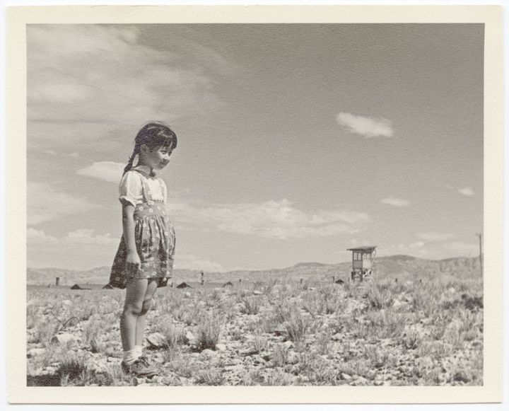 Inscribed on the back of the photo: "Young girl near guard tower-Ayaho Inouye". She is standing near a guard tower in the barren desert that was home to the Heart Mountain concentration camp.