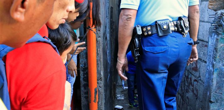 Residents look on as a police investigator inspects the body of a suspected drug pusher, along an alley in Quezon city. 
