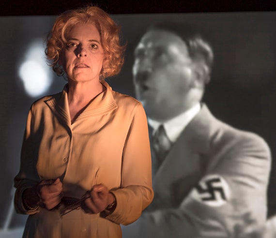 Stacy Ross as Leni Riefenstahl, defending herself; behind her, an image from <em>Triumph of the Will</em>