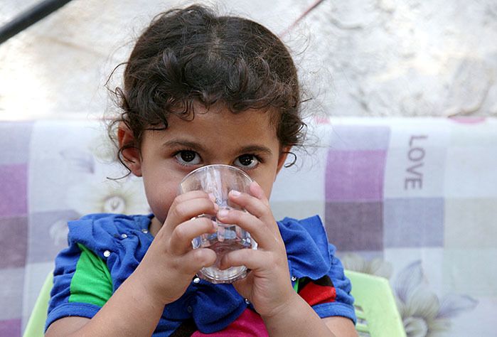 Mayar drinks clean water at home after the installation of a water network at her home in Gaza.