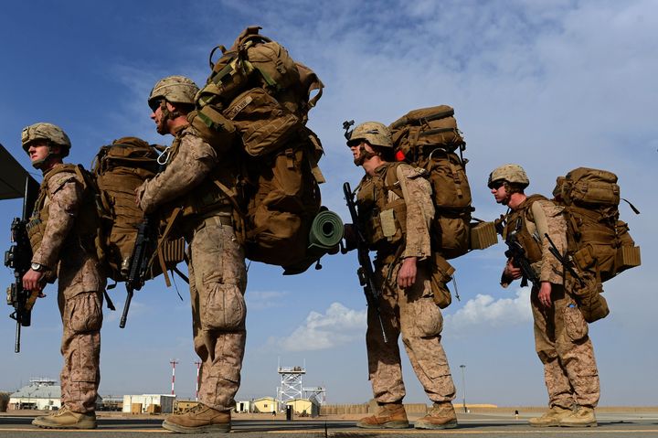 Marines individually carry heavy loads as they wait to board an aircraft in Afghanistan.