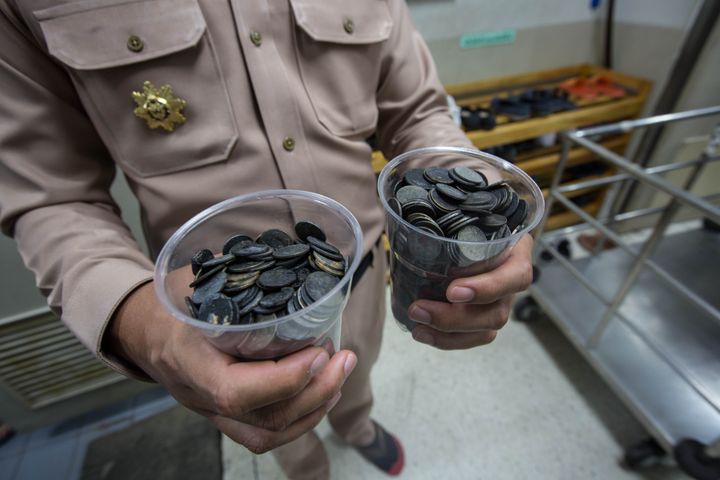 An officer holds up two cups containing some of the coins the turtle had consumed over the years.