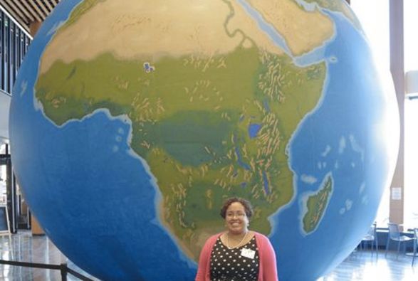 Natacha Scott, the social studies director for Boston Public Schools, stands before a massive globe that shows the continent of Africa. 