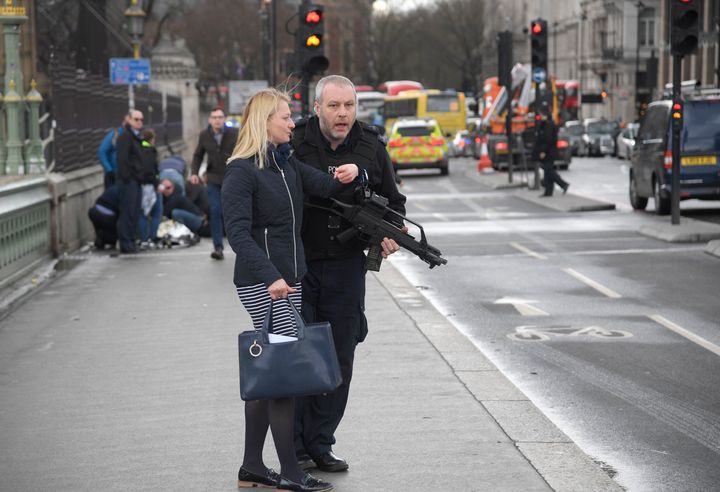 An armed police officer assists a member of the public on Westminster Bridge