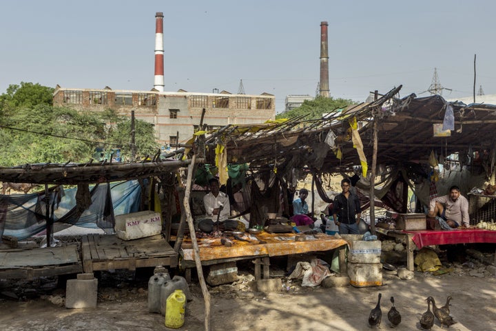 Vendors sit at stalls as smokestacks stand in the background at a coal-fired power plant in Badarpur, Delhi, India, on M