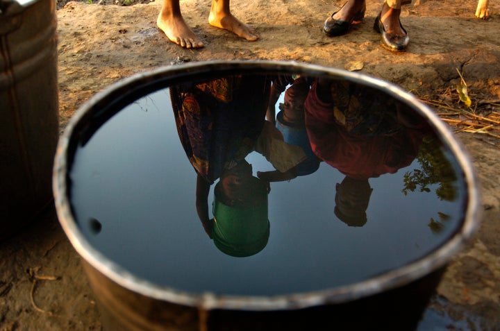 Young women in Malawi, Africa, are reflected in a bucket of water as they prepare to make the long hike back to their homes after filling their bucket with water. This was already their second trip for the morning to gather water and this was 6:30 am.